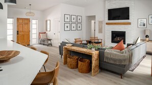 Una sala de estar moderna con chimenea, un comedor con mesa blanca y un sofá con manta.