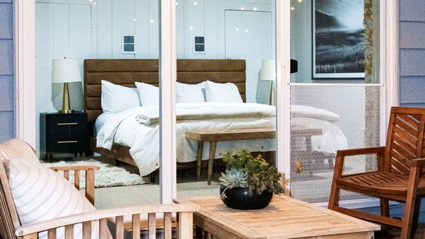 Een slaapkamer met een bed, nachtkastje, lamp en een groot raam.