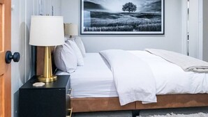 Een slaapkamer met een bed, een nachtkastje met een lamp, een lijst met een landschapsafbeelding en een zacht vloerkleed.