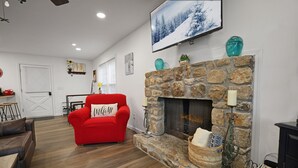 A living room with a stone fireplace, a red sofa with a 'Welcome' pillow, a mounted TV, and a bookshelf. - Escape to Beech Mtn-0.6 mi to Ski Lodge-Walkable (Beech Mountain)