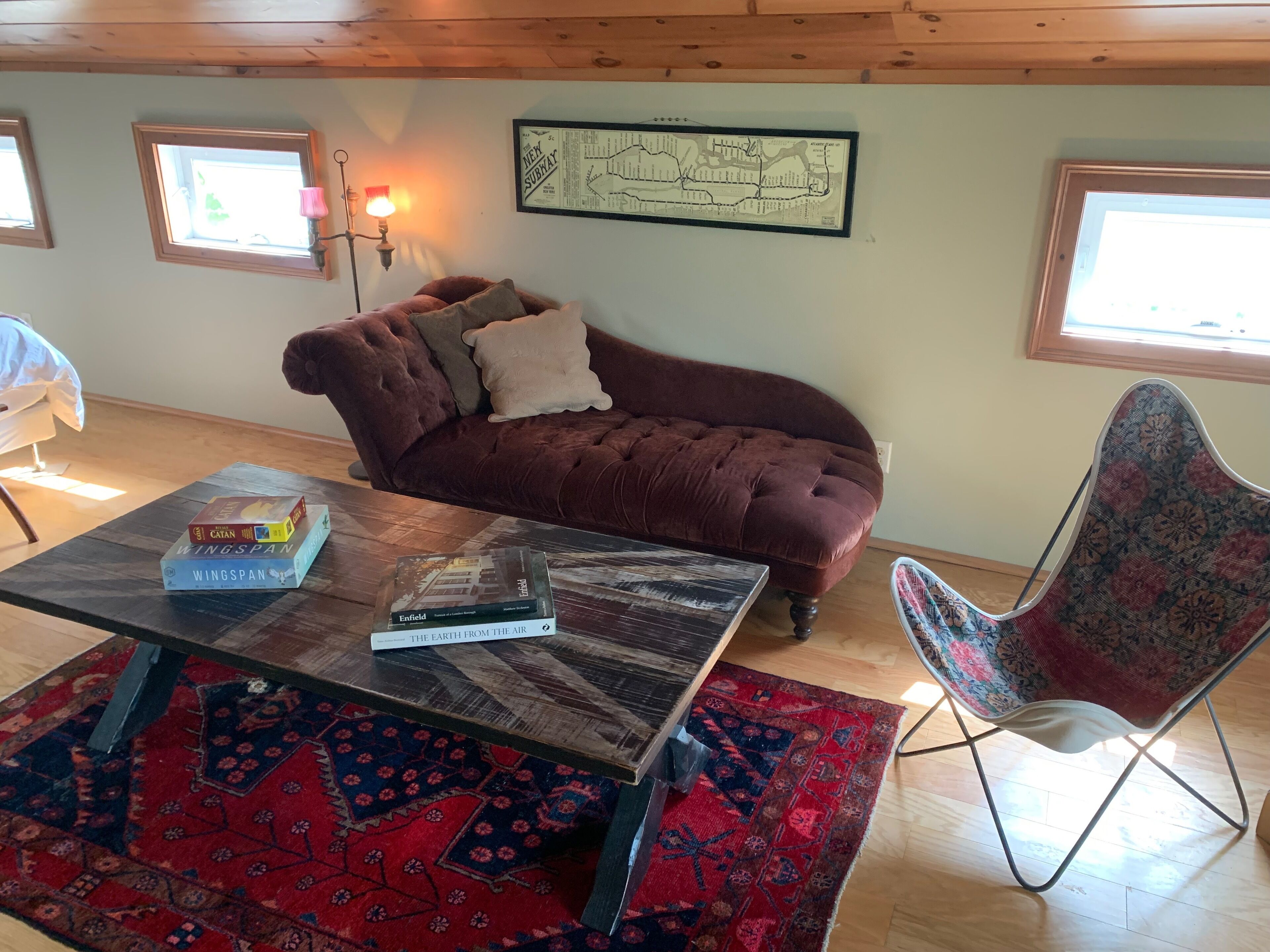 A cozy living room with a brown sofa, a patterned rug, a coffee table with books, and a map on the wall.