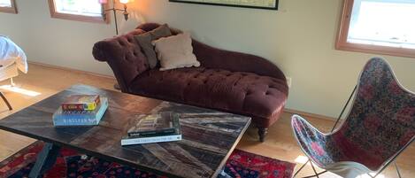 A cozy living room with a brown sofa, a patterned rug, a coffee table with books, and a map on the wall.