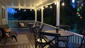 A covered outdoor deck with wooden flooring, white railings, and string lights. - CREEKSIDE RETREAT 5 miles from Cooperstown, NY. (Hartwick)