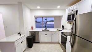 Eine moderne Küche mit weißen Schränken, einem Edelstahl-Kühlschrank und einem Fenster mit Blick nach draußen.