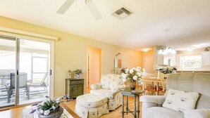A living room with a sofa, ottoman, and a table with a vase of flowers. There is a dining area with chairs and a table in the background. - Complimentary Golf Cart! Home in The Villages (The Villages)