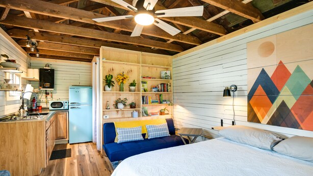 A cozy room with a bed, a blue sofa, a kitchen area, and a wooden ceiling.