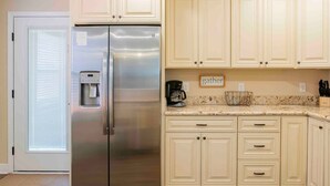 Una cocina con armarios de color claro, un refrigerador de acero inoxidable, una cafetera y un cartel con la palabra 'gather'.