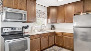 A kitchen with wooden cabinets, stainless steel appliances, a window with blinds, and a patterned rug. - Cozy Coleman-Families- Near Beaches, Airport & PCC (Pensacola)
