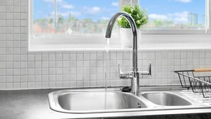 Een keuken met een roestvrijstalen spoelbak, een moderne kraan en een raam met uitzicht op gebouwen.