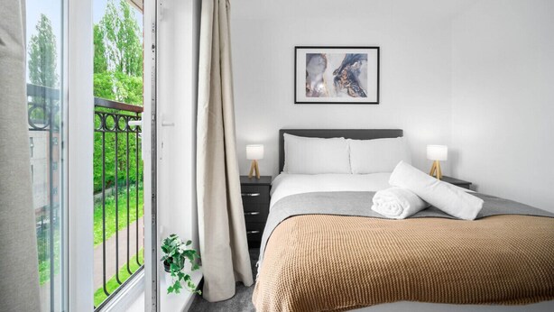 Een slaapkamer met een bed, nachtlampjes, een kunstwerk in een lijst en uitzicht op groen.