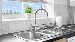 Een moderne keuken met een roestvrijstalen spoelbak, een plant in een pot en een raam met zonwering.