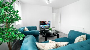 Een moderne woonkamer met smaragdgroene banken, een glazen salontafel, een flatscreen televisie en een potplant.