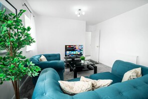 Ein modernes Wohnzimmer mit türkisfarbenen Sofas, einem Glastisch, einem Flachbildfernseher und einer Topfpflanze.