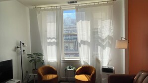 Un salon équipé d’un téléviseur à écran plat, de deux fauteuils orange, d’un canapé en cuir marron, d’une table basse ronde et d’une plante en pot.