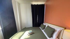 Un lit bien fait, avec une literie verte, des oreillers blancs et une petite serviette posée sur le côté.