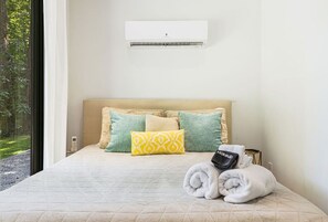 A hotel room with a bed, pillows, a towel, a robe, and an air conditioning unit.
