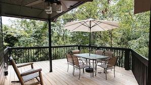 A wooden deck with a table and chairs, an umbrella, and a rocking chair.