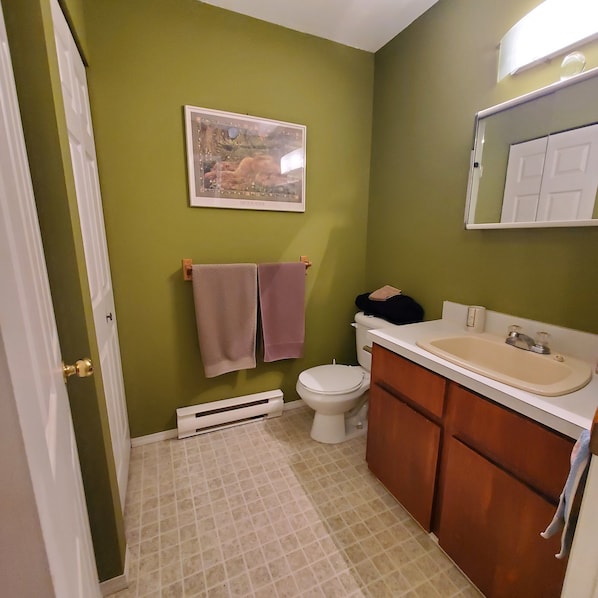 Une salle de bain avec des murs verts, des toilettes blanches, un lavabo beige et un meuble en bois.