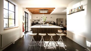 A modern kitchen with a central island, bar stools, and a large window providing natural light. - Vakantiehuis Zand7 (Lommel)