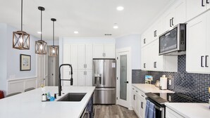 A modern kitchen with white cabinets, a stainless steel refrigerator, a built-in oven, and a black backsplash.