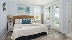 A bedroom with a large bed, a ceiling fan, a nightstand with a lamp, and a window with shutters.