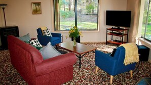 Una sala de estar con un sofá rojo, sillones azules, una mesa de centro y un televisor sobre un mueble.
