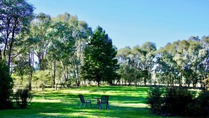Un parque con césped, con dos sillas y una mesa, rodeado de árboles.