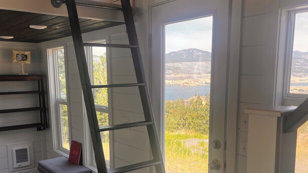 A room with a wooden ceiling, a ladder leaning against a door, a bench, and a view of a lake and mountains through the door. - Tiny Home, Lake View, RV & Boat Parking, Pistol Range. (davenport)