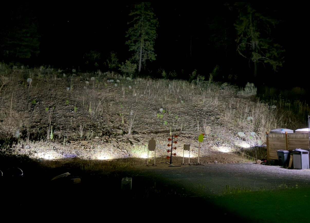 Ein Außenbereich bei Nacht mit einem Feldweg, einer kleinen Struktur und etwas Grün.