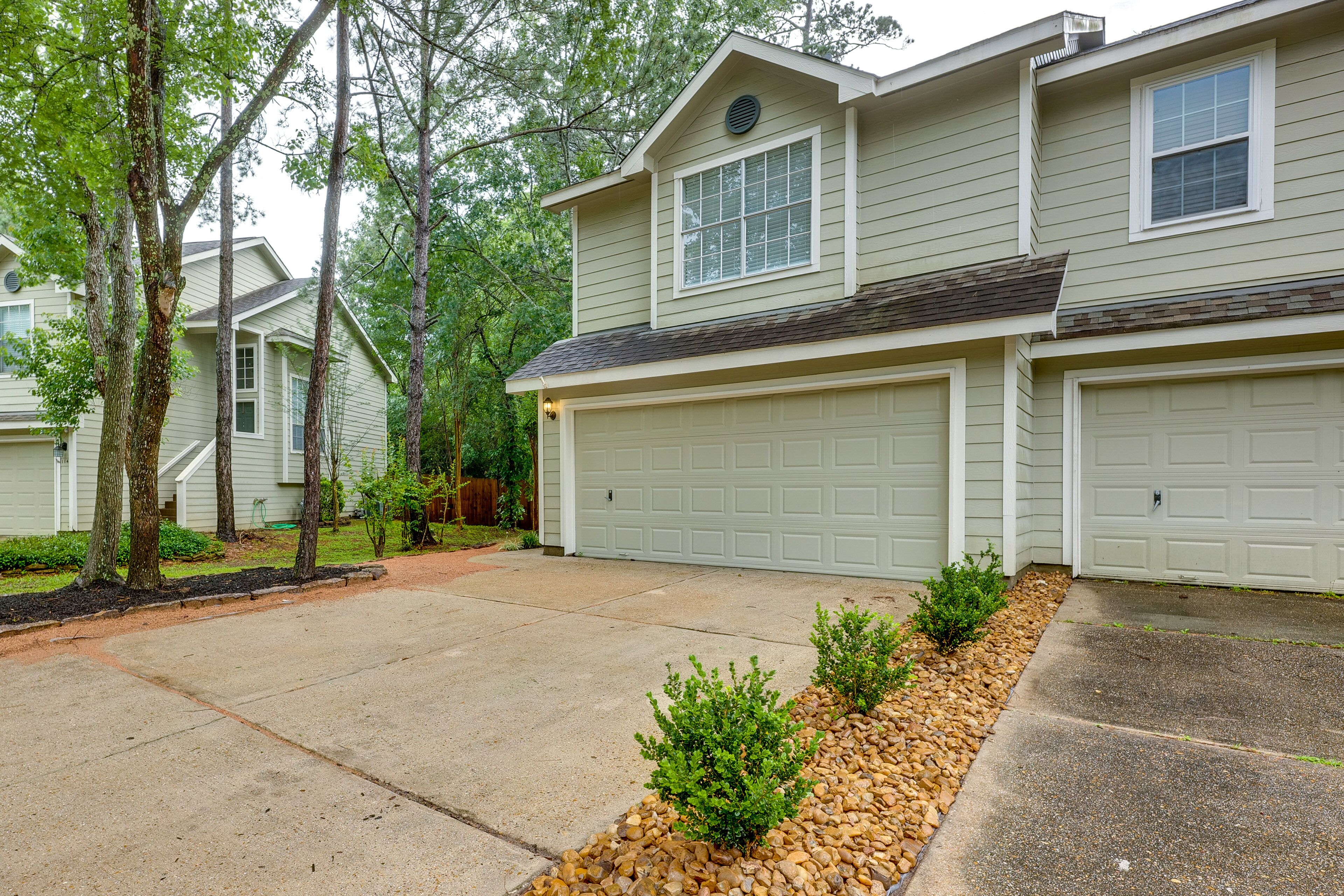 A two-story house with a garage, a driveway, and a landscaped area with small bushes and a gravel border.