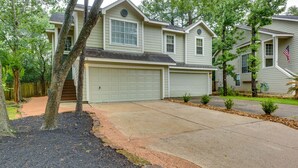 A two-story house with a garage, surrounded by trees and a well-maintained lawn. - Modern Woodlands Townhome w/ Spacious Yard & Patio (The Woodlands)