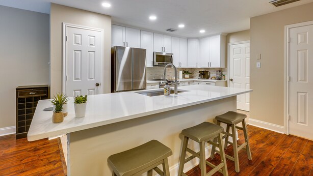 A modern kitchen with white cabinets, stainless steel appliances, and a large island with stools. - Modern Woodlands Townhome w/ Spacious Yard & Patio (The Woodlands)
