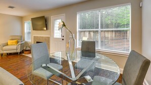 A modern living room with a glass coffee table, comfortable seating, a fireplace, and large windows with blinds. - Modern Woodlands Townhome w/ Spacious Yard & Patio (The Woodlands)