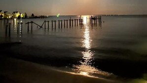 A nighttime beach scene with a calm sea, a wooden pier, and distant buildings with lights. - Entire house on quiet street w/fenced yard—1 block from river, 3 from bay (Annapolis)