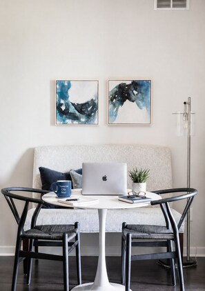 Een moderne kamer met een witte bank, twee abstracte schilderijen, een laptop, een koffiemok, een plant en een hoge vloerlamp.