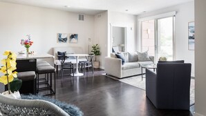 Un salon moderne avec un canapé, une table à manger et une table basse. On trouve une plante sur la table basse et un vase de fleurs sur la table à manger.