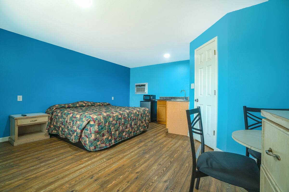 A room with a bed, a desk, a chair, and a kitchenette.