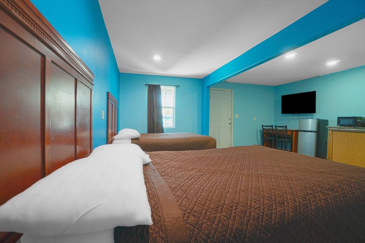 A hotel room with a large bed, a desk with a chair, a television, and a door.