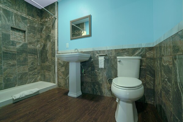 A bathroom with a bathtub, sink, and toilet, featuring marble walls and wooden flooring.