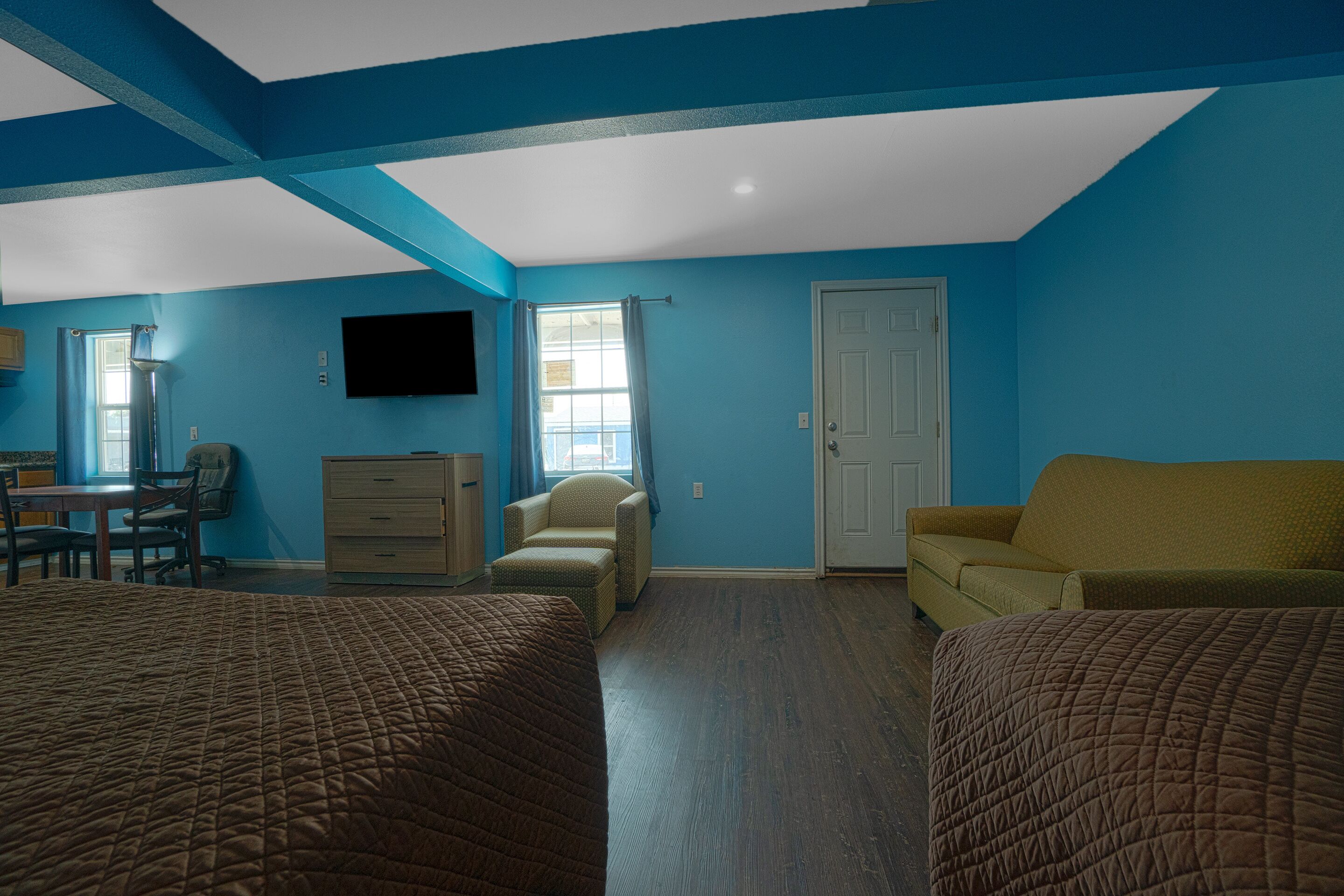 A room with two beds, a desk, a chair, a television, and a door.