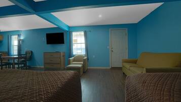 A room with two beds, a desk, a chair, a television, and a door.
