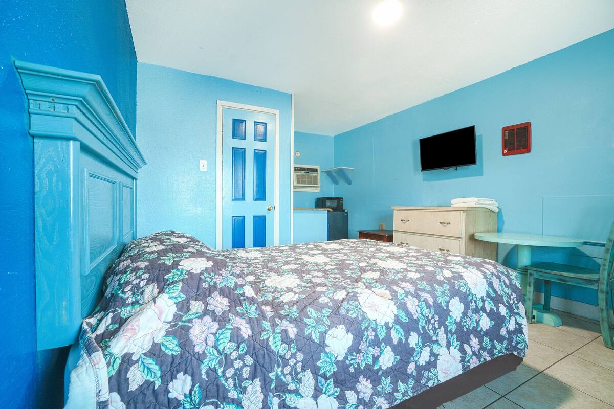 A bedroom with a floral bedspread, a blue door, a television, and a small table.