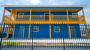 A two-story building with a blue and yellow exterior, a balcony on the upper floor, and a gated entrance. - Plaza Motel Corpus Christi By Oyo (Corpus Christi)
