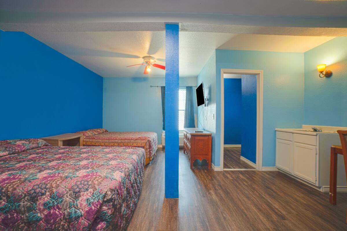 A room with two beds, a ceiling fan, a dresser, and a desk.