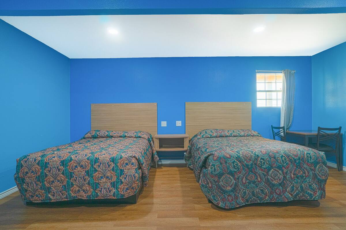 A room with two beds, a small table, and a window with curtains.