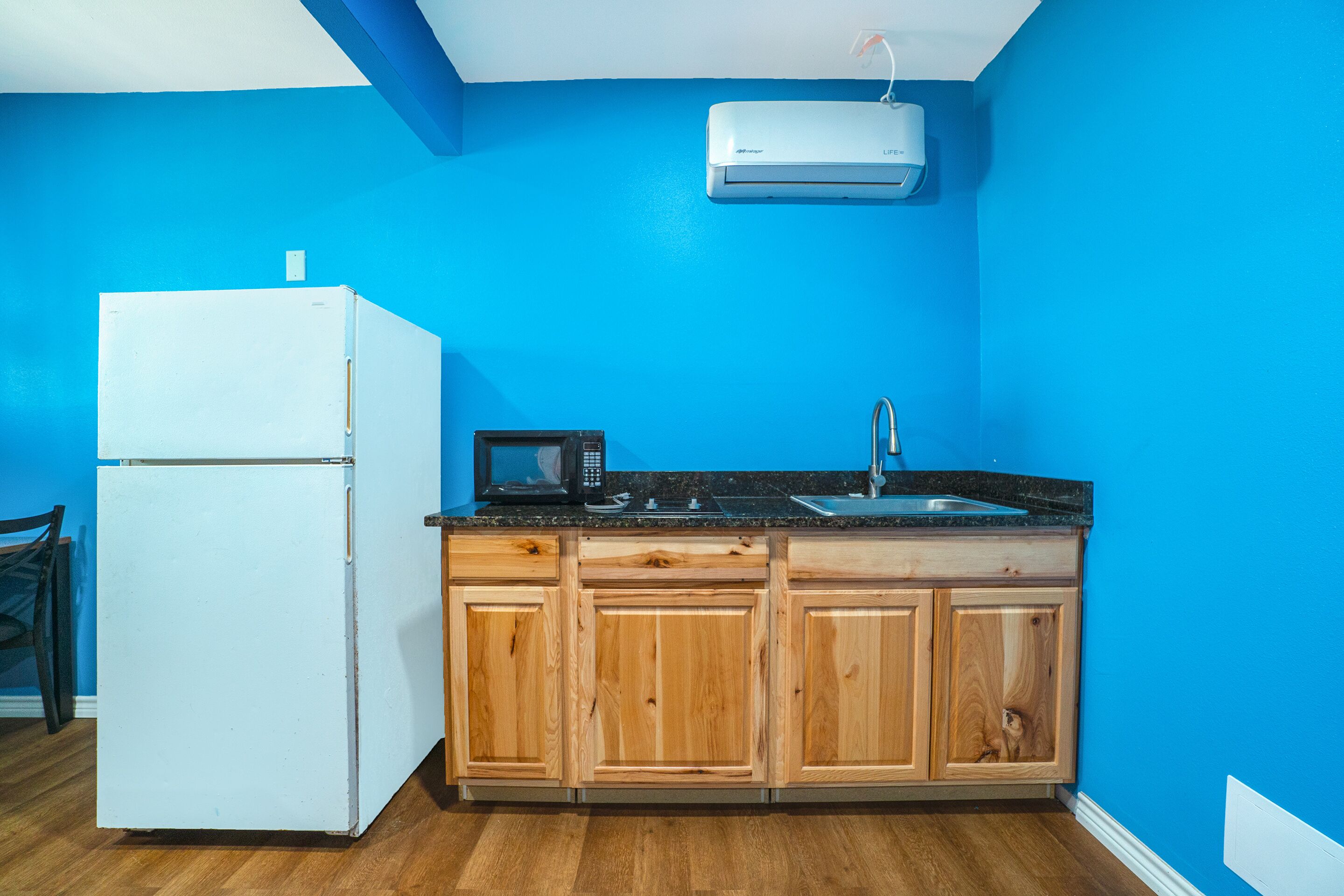 A kitchen with a white refrigerator, wooden cabinets, a black countertop, a microwave, and a sink.