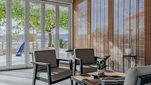 A modern indoor space with large glass doors leading to an outdoor area, featuring a wooden table, two chairs, and a small plant. - Villa Ponar with Swimming Pool (Kuciste)