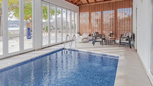 A swimming pool with clear glass walls, wooden ceiling beams, and outdoor seating area with chairs and a table. - Villa Ponar with Swimming Pool (Kuciste)