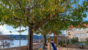 A playground with a slide and swings, located near a body of water and a stone building. - Villa Ponar with Swimming Pool (Kuciste)