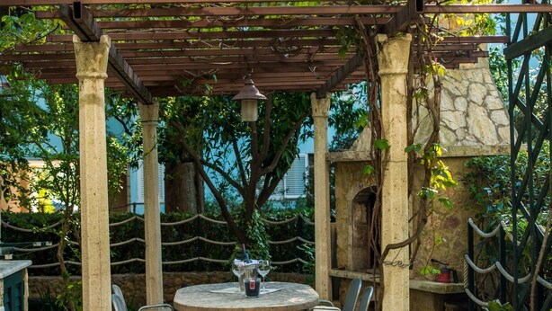 An outdoor patio with a round stone table and blue cushioned chairs, surrounded by stone pillars and a pergola. - Green Terrace Apartment I (Dubrovnik)
